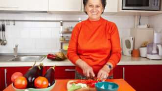 A smiling older woman cutting produce in a kitchen. | Xalanx | Dreamstime.com