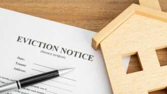 An eviction notice and a toy wooden house. | Avictorero | Dreamstime.com