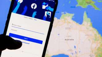A smartphone on the Facebook login screen, against a world map of Australia in the background. | Serazahmed99 | Dreamstime.com