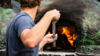 A cook shovels a pizza into a wood-fired stone pizza oven. | Lightpoet/Newscom