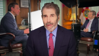 John Stossel is seen in front of a still from his interview with Gov. Ron DeSantis | Stossel TV